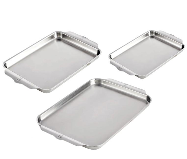Three Hestan Provisions OvenBond Sheet Pans, made of triple-bonded clad stainless steel, are arranged diagonally on a white background. These versatile pans are oven safe up to 600°F for all your baking needs.