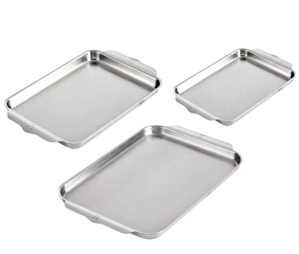 Three Hestan Provisions OvenBond stainless steel baking trays of varying sizes are arranged with handles visible.