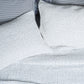 Two white pillows and a matching organic cotton coverlet from the John Robshaw Hand-Stitched Bedding Collection, featuring a subtle stitched pattern, arranged neatly on a textured background.