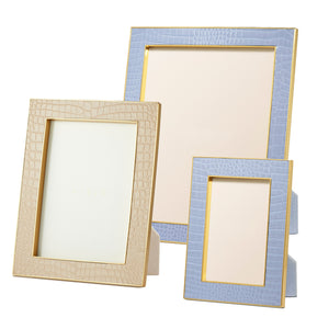 Three empty rectangular frames from Aerin’s Classic Croc Leather Frame Collection, crafted from Italian croc-embossed leather in beige and light blue, stand upright against a white background.
