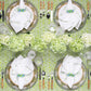 Table set for four with white napkins, woven placemats, bamboo-handled cutlery, clear glassware, and a Kim Seybert Alfresco Tablecloth featuring Indian block printing on 100% cotton, topped with a hydrangea centerpiece.