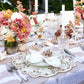 A formal table is set with floral centerpieces, crystal glassware, seashell decor, candles on a beige tablecloth, and white napkins accented by the Kim Seybert Beachcomber Napkin Ring Set.