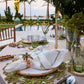 Elegant outdoor dining set with nature-inspired decor, green glassware, white napkins featuring the Kim Seybert Palm Coast Napkin Ring (Set of 4), and a pool with string lights in the background.