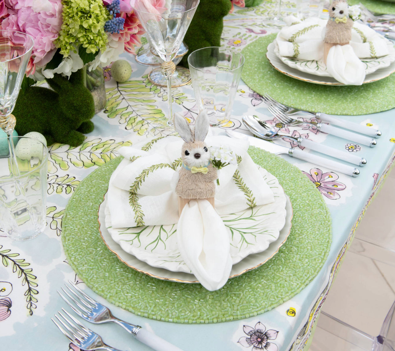 A spring table is set with the Kim Seybert Easter Bunny Napkin Ring on layered green-patterned plates, surrounded by glassware, cutlery, and florals—perfect for a charming seasonal decor.