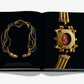 An Assouline book, "Uzbekistan: Masterpieces of the Silk Road," is open, presenting images of gold jewelry reminiscent of historical treasures: a multi-strand necklace on the left and an archaeological artifact with a red gemstone set in gold on the right, celebrating Uzbekistan's rich heritage.