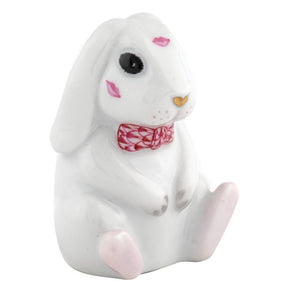 The Herend "Bunny Kisses" collectible is a handcrafted porcelain bunny from Hungary with pink lip prints, a red patterned bow tie, and pink-tipped paws, seated upright.