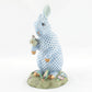 The Herend Reserve Collection Anniversary Bunny is a hand-painted porcelain figurine depicting a standing rabbit with blue and white patterns, holding a decorated egg on a grassy, flowered base. Inspired by classic Herend designs.