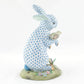 The Herend Reserve Collection Anniversary Bunny is a blue and white porcelain rabbit with a small bird, standing on a floral green base with a butterfly, featuring exquisite hand-painted designs inspired by classic Herend porcelain.