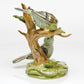 The Herend Reserve Collection The Rothschild Birds figurine features two green porcelain songbirds on a light brown branch with a green base, accented by a butterfly and delicate flowers.