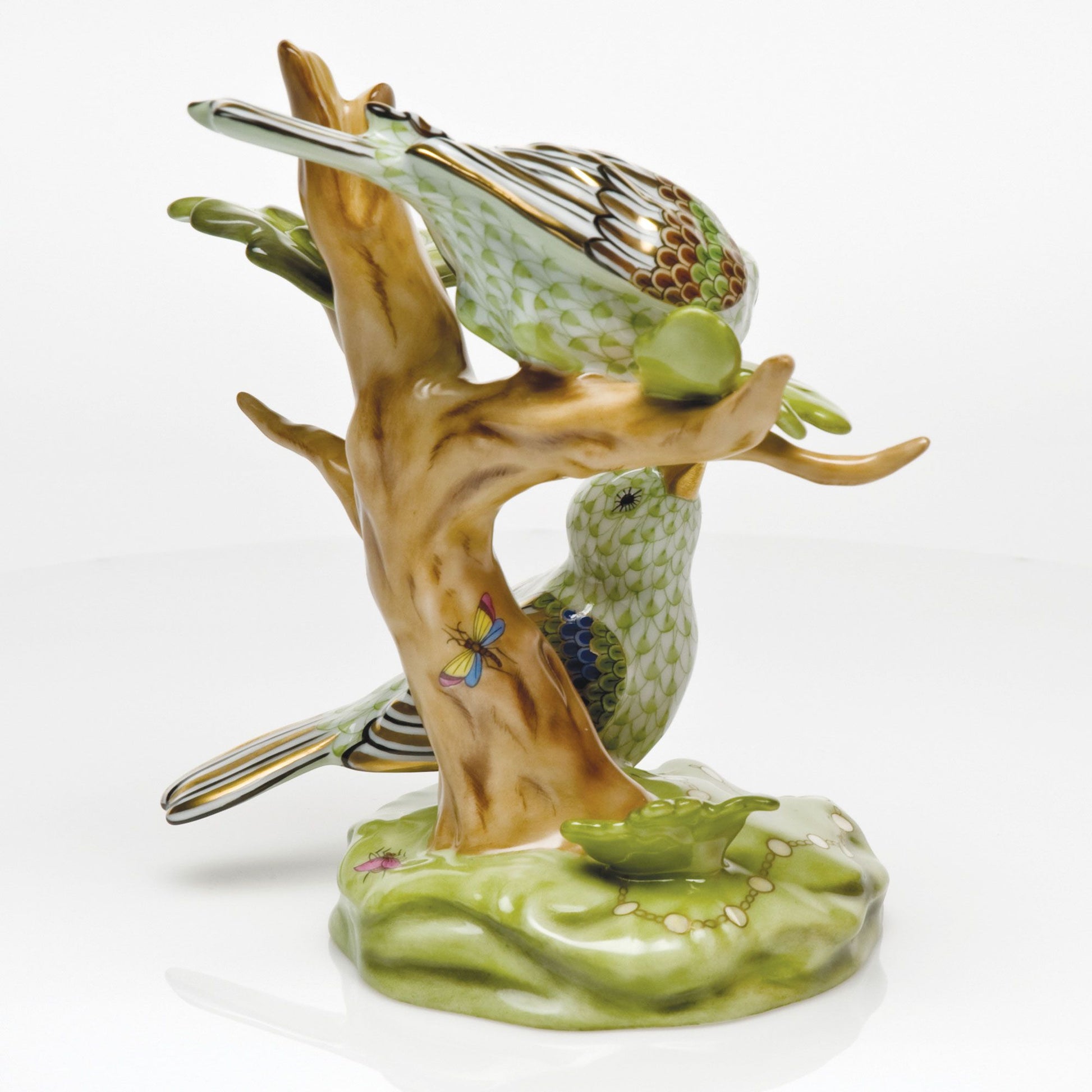 The Herend Reserve Collection The Rothschild Birds figurine features two green porcelain songbirds on a light brown branch with a green base, accented by a butterfly and delicate flowers.