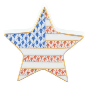 The Herend Patriotic Star is a porcelain dish shaped like a star, featuring a stylized American flag with blue and red fish scale patterns and gold accents—a collectible decorative piece for any space.