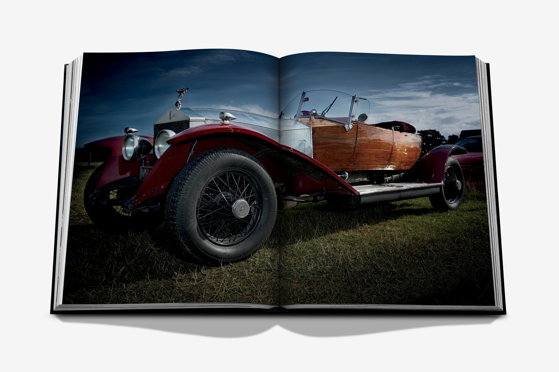 A striking tribute to automotive history and luxury photography, Vintage Cars (2nd Edition) by Assouline features a dramatic photo of a vintage convertible with wood paneling displayed across an open book, viewed from a low angle outdoors.