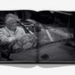 A black and white photograph of an older man in a racing suit seated in a vintage race car is featured on the open pages of Vintage Cars (2nd Edition) by Assouline, set against a white background—a timeless image that embodies the essence of automotive history.
