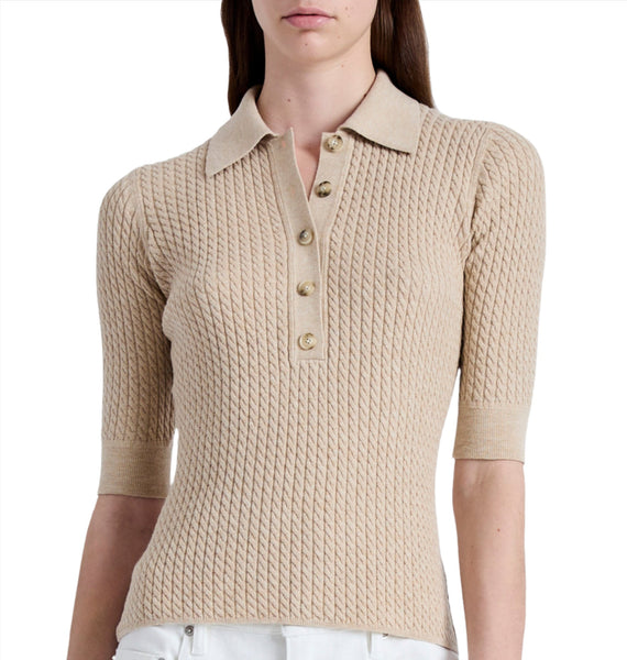 A woman dressed in the Proenza Schouler Sera Knit Polo, featuring a beige color, short sleeves, and an elegant slim fit with button detailing and knit trims, paired with white pants.