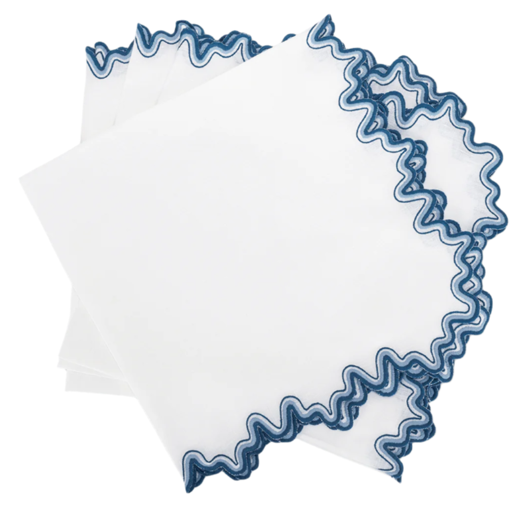 Three linen handkerchiefs from Matouk’s Wave Tabletop Collection, Aquarius, with wavy blue embroidery, are stacked in a fan on a plain background. Crafted to OEKO-TEX Standard 100, they’re perfect for an elegant embroidered tabletop setting.