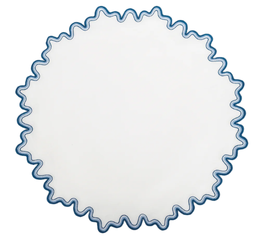 The Matouk Wave Tabletop Collection, Aquarius, features a round white plate with a blue wavy edge—ideal for pairing with linen napkins or an embroidered tablecloth for an elegant dining touch.