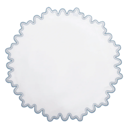 The Matouk Wave Tabletop Collection in Hazy Blue features a round white linen tabletop with a wavy blue embroidered edge and is OEKO-TEX certified for safety and style.