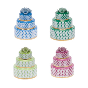 The Herend Wedding Cake collection features four three-tiered cakes in blue, green, light green, and pink with decorative flowers, hand-painted designs inspired by Herend porcelain, geometric patterns, and gold accents on a white background.