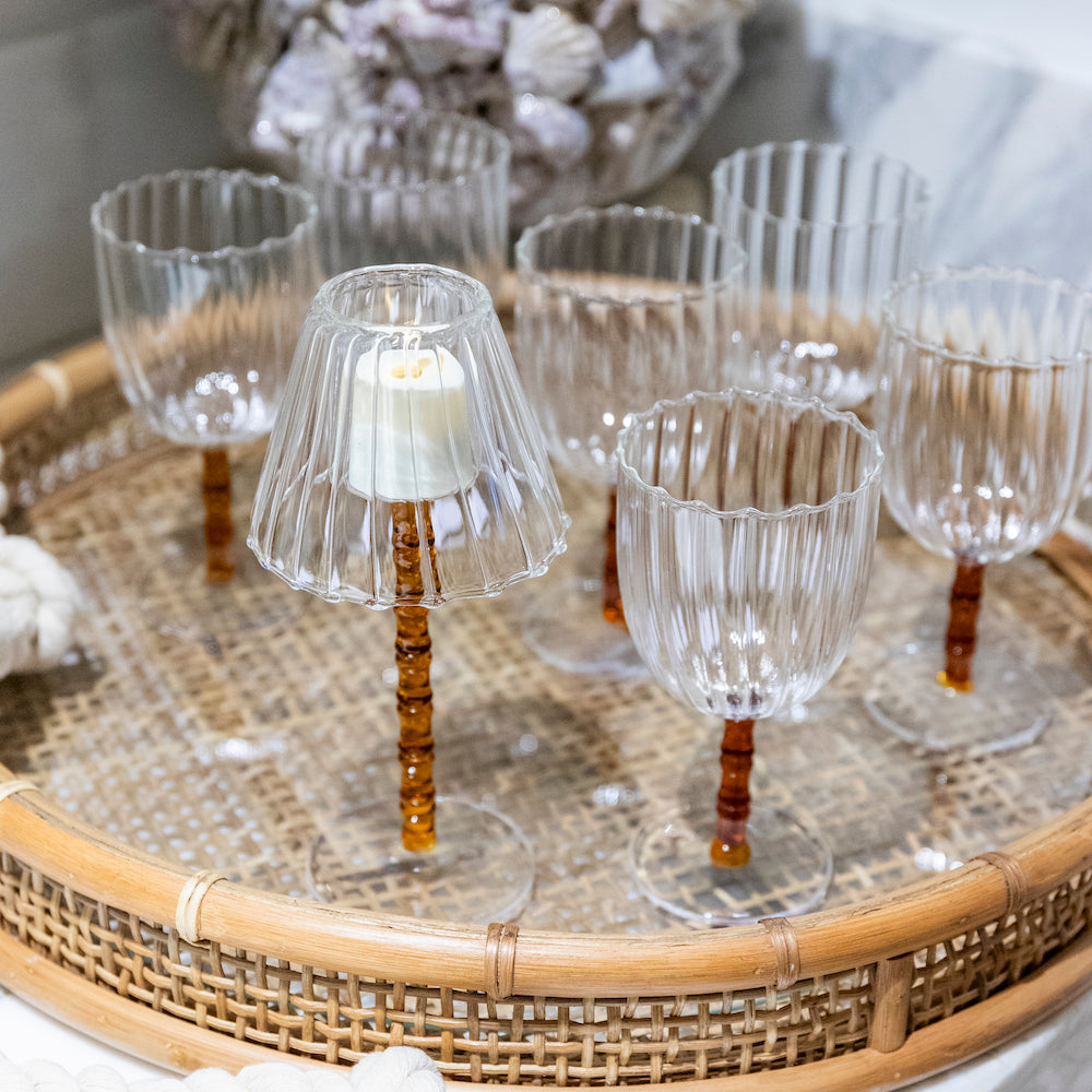 The Rivoli Drinkware and Tealight Collection by Ichendorf Milano features clear, ribbed wine glasses with amber stems, including a fluted glass tealight holder—hand-crafted glassware perfect for distinctive decor or entertaining.