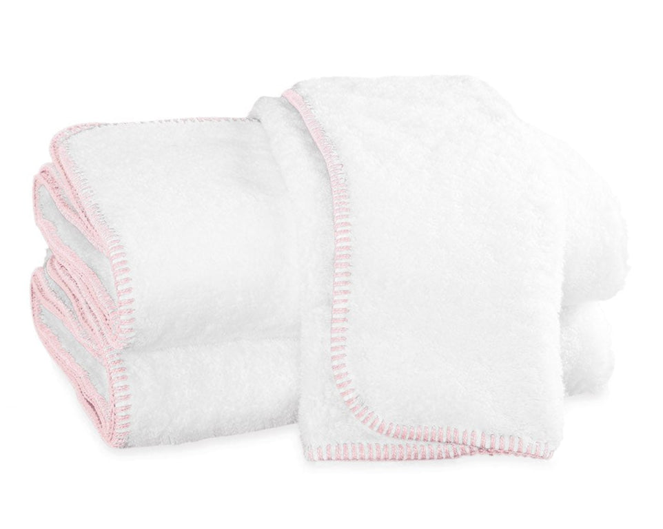 Three white towels with light pink terry whipstitching from the Matouk Whipstitch Bath Collection are neatly folded and stacked on a white background.
