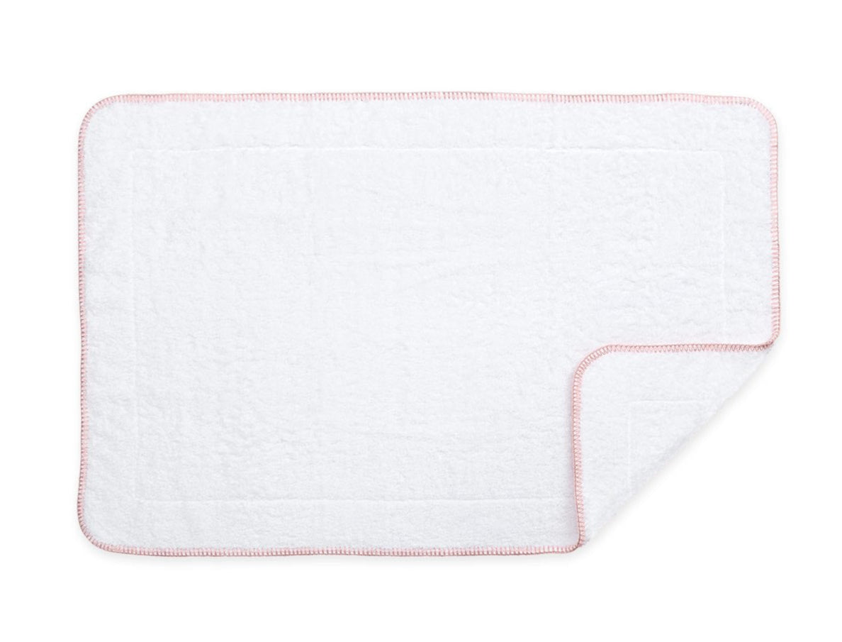 A rectangular white towel from Matouk's Whipstitch Bath Collection, made with Cairo long-staple cotton and finished with a light pink whipstitched border, shown flat with one corner gently folded.