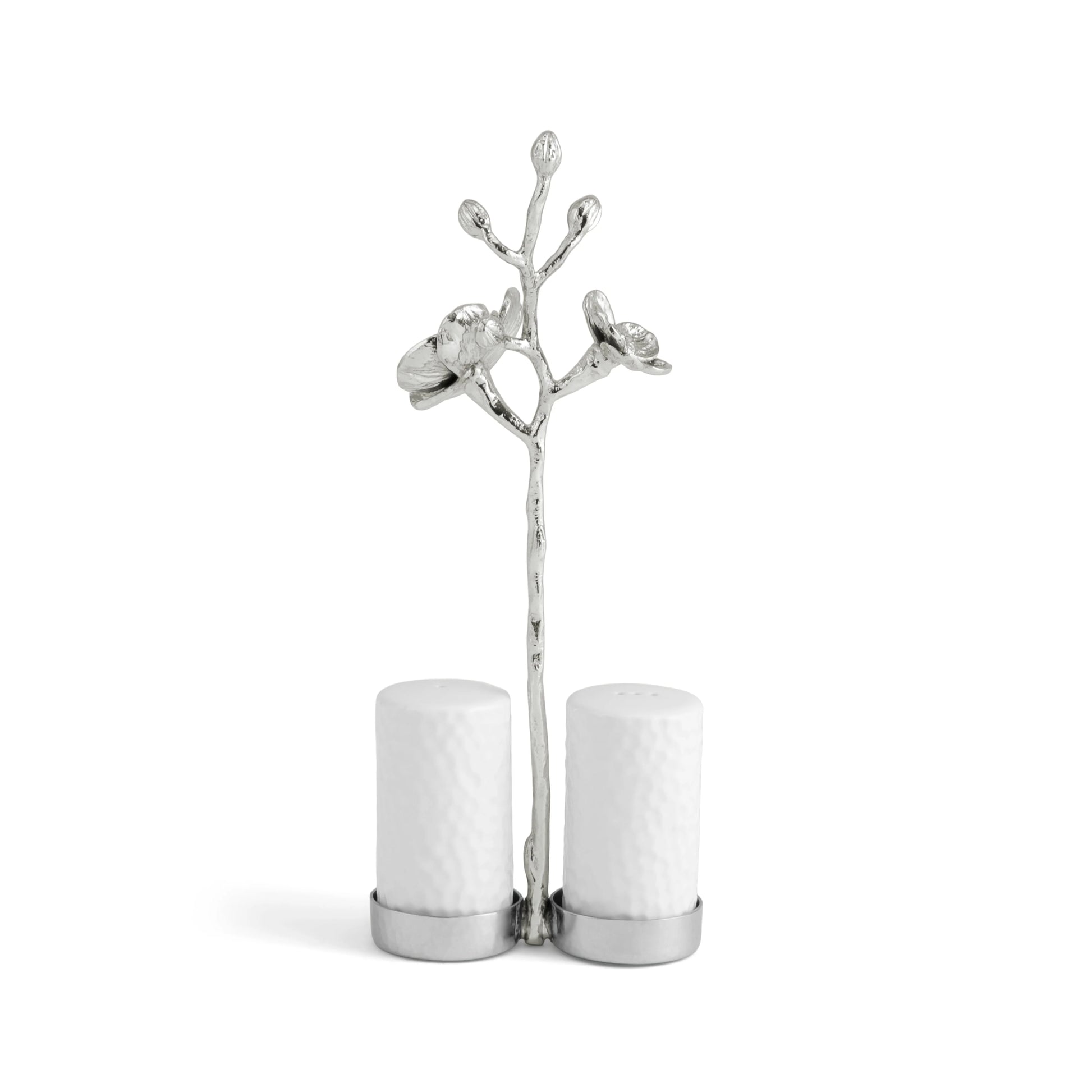 The Michael Aram White Orchid Serveware Collection features white ceramic salt and pepper shakers in a silver, flower-adorned branch holder, capturing purity and subtle mystery against a plain white background.