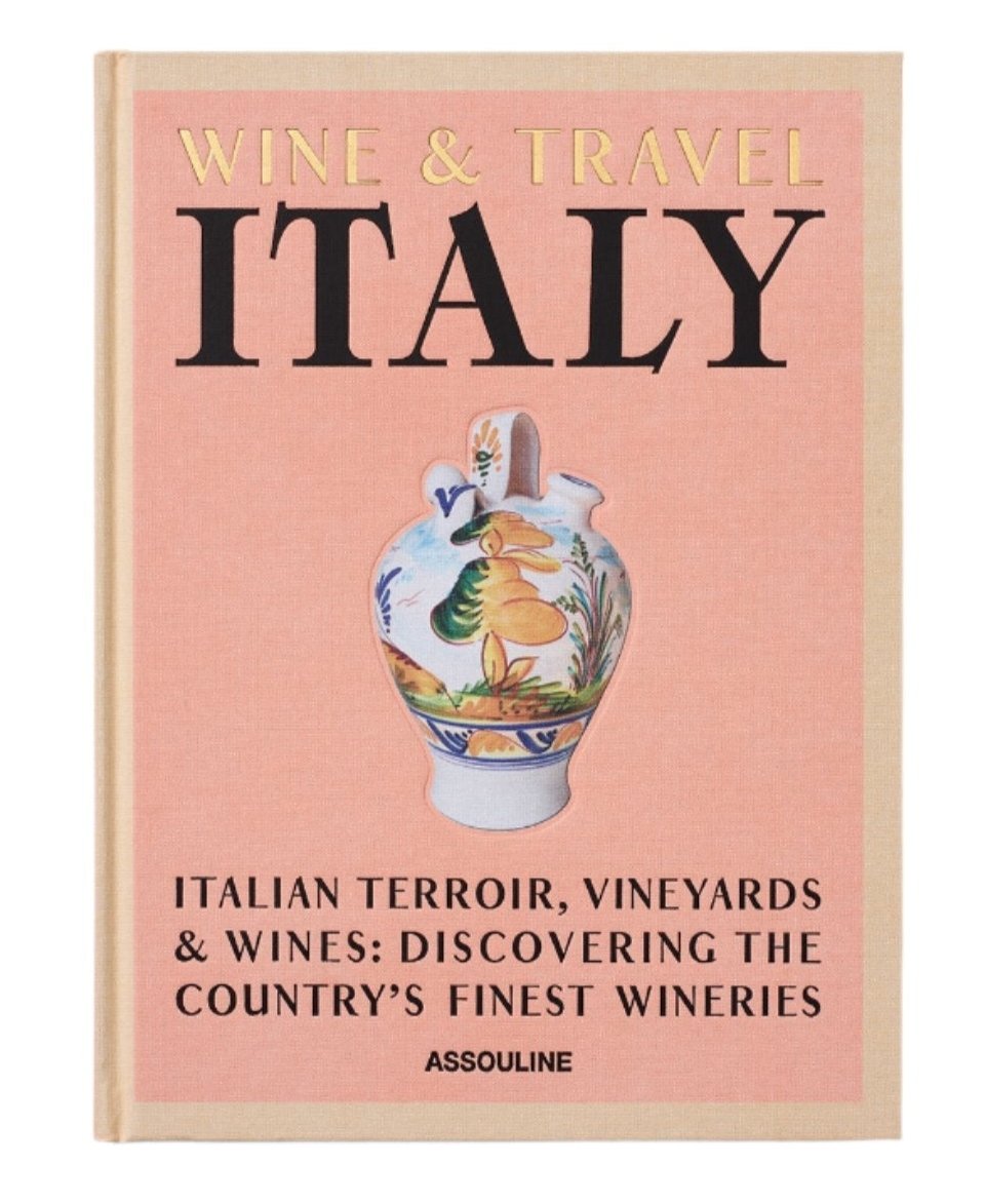The book cover titled "Wine & Travel Italy" from Assouline showcases an illustrated vase adorned with a scenic design. The subtext, "Italian Terroir, Vineyards & Wines: Discovering the Country's Finest Wineries" by Enrico Bernardo, pays homage to Italian vineyards and wine tourism experiences.