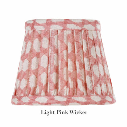 The Zafferano x Fermoie Poldina Lampshade Collection by Zafferano America offers a pleated design with a light pink wicker pattern and white ovals on textile, capturing the elegance of Fermoie's style.