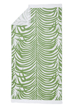 The Zebra Beach Towel Collection by Matouk features a rectangular towel with a green tropical leaf pattern on white, accented with white fringe on the short edges.