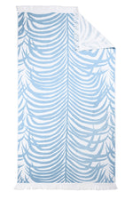 The Matouk Zebra Beach Towel Collection features a rectangular white towel with light blue zebra-stripe tropical leaves, fringe on two edges, and a folded corner revealing the reverse side.