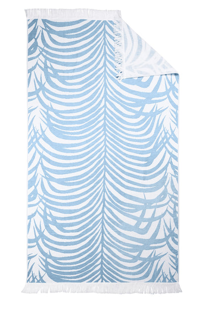 The Matouk Zebra Beach Towel Collection features a rectangular white towel with light blue zebra-stripe tropical leaves, fringe on two edges, and a folded corner revealing the reverse side.