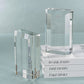 The Zodax Claire Crystal Glass Bookend Set holds and flanks three white books titled "WORK HARD," "DREAM BIG," and "TAKE RISKS" for elegant bookshelf decor on a light blue surface.