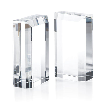 The Claire Crystal Glass Bookend Set by Zodax features two clear rectangular glass blocks with sharp edges and clean lines, serving as elegant minimalist bookends and a sophisticated addition to any bookshelf decor.