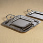 The Manetta Polished Nickel Tray Collection by Zodax features three elegant serving trays with handles, stacked on a beige textured surface for a refined decorative touch.