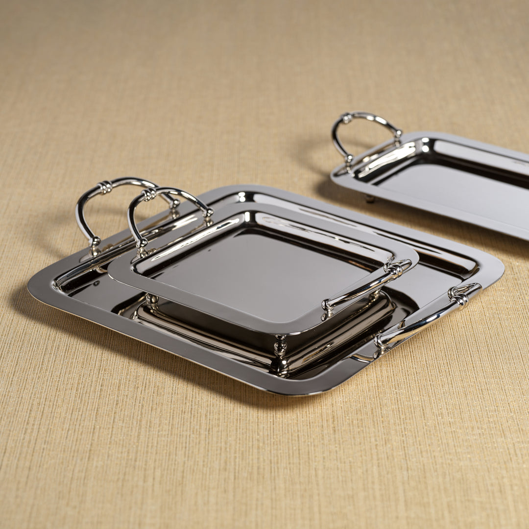 The Manetta Polished Nickel Tray Collection by Zodax features three elegant serving trays with handles, stacked on a beige textured surface for a refined decorative touch.