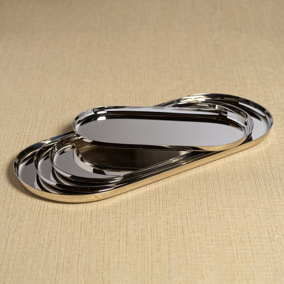 The Park Lane Oval Tray Collection by Zodax features three polished nickel trays, each nested on a textured beige surface, adding elegant style as a decorative set.