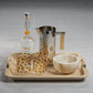 A bottle of 44° North vodka, two patterned glasses, a metal pitcher, and a decorative bowl are arranged on the Zodax Airelles Raffia and Chambray Serving Tray for a stylish presentation.