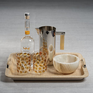A bottle of 44° North vodka, two patterned glasses, a metal pitcher, and a decorative bowl are arranged on the Zodax Airelles Raffia and Chambray Serving Tray for a stylish presentation.