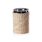 A glass jar from the Zodax Palmier Barware Collection, featuring a shiny metal lid and hand-woven rattan wrap, stands upright against a white background in this elegant display.