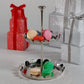 The Zodax Scalloped Two-Tier Tray Collection displays vibrant macarons, while wrapped gift boxes sit behind on a sparkling surface.