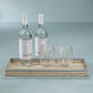 Two clear water bottles and two patterned glasses are arranged on a Zodax La Côte Coiled Rectangular Tray, made from abaca fibers, set against a pale blue background.