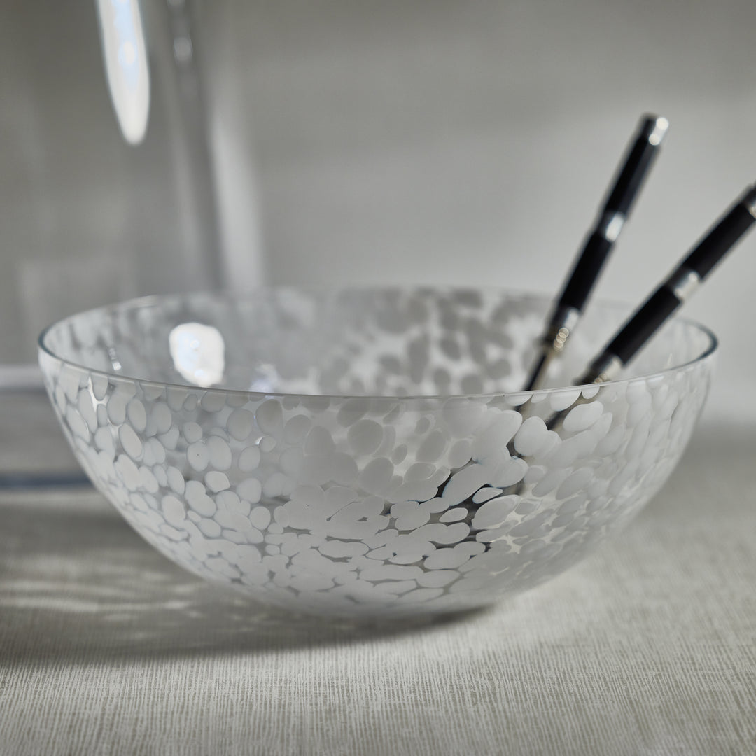 The Zodax Liguria Confetti Bowl, made of patterned glass with a white dappled design, rests on a light surface; inside lie two black chopsticks with white tips—an elegant accent for any setting.
