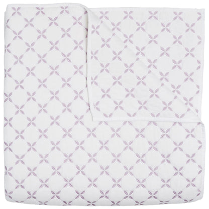 The John Robshaw Layla Lavender Coverlet is a white cotton voile quilt featuring intersecting lavender circles and floral motifs inspired by Mughal gardens, shown neatly folded with one corner turned down.