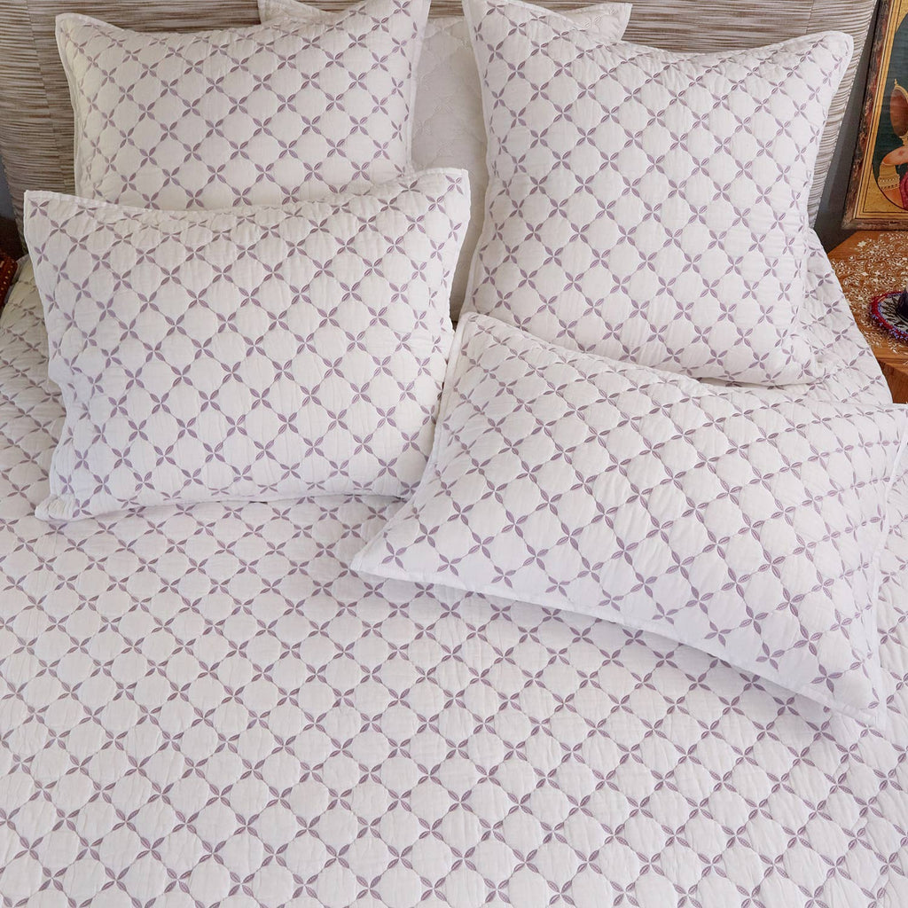 A neatly made bed with the John Robshaw Layla Lavender Coverlet and five matching pillows, all showcasing a subtle gray geometric pattern on white cotton voile.