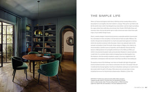 A modern dining room with a round wooden table surrounded by green velvet chairs, curated by an interior designer inspired by "Kathryn Ireland: A Life in Design" from Simon & Schuster. A large window with closed curtains is on one side, while a sideboard and various decor items are arranged around the room.