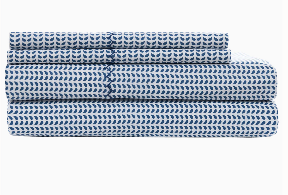 A neatly folded sheet set from the John Robshaw Cinde Bedding Collection in Light Indigo and white, displaying a repeating leaf-like Cinde print, including two pillowcases, a flat sheet, and a fitted sheet, stacked on a white background.