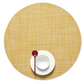 A Chilewich Round Placemat from the Chilewich brand, made with phthalate-free Terrastrand yarns, displays a Mini Basketweave texture and holds a white bowl and saucer set with a red spoon on top.