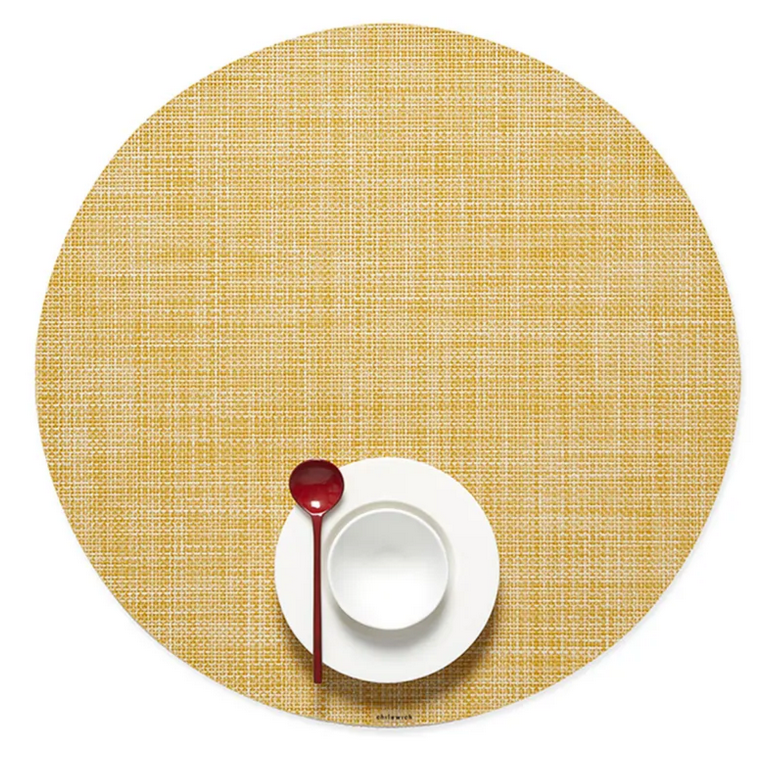 A Chilewich Round Placemat from the Chilewich brand, made with phthalate-free Terrastrand yarns, displays a Mini Basketweave texture and holds a white bowl and saucer set with a red spoon on top.