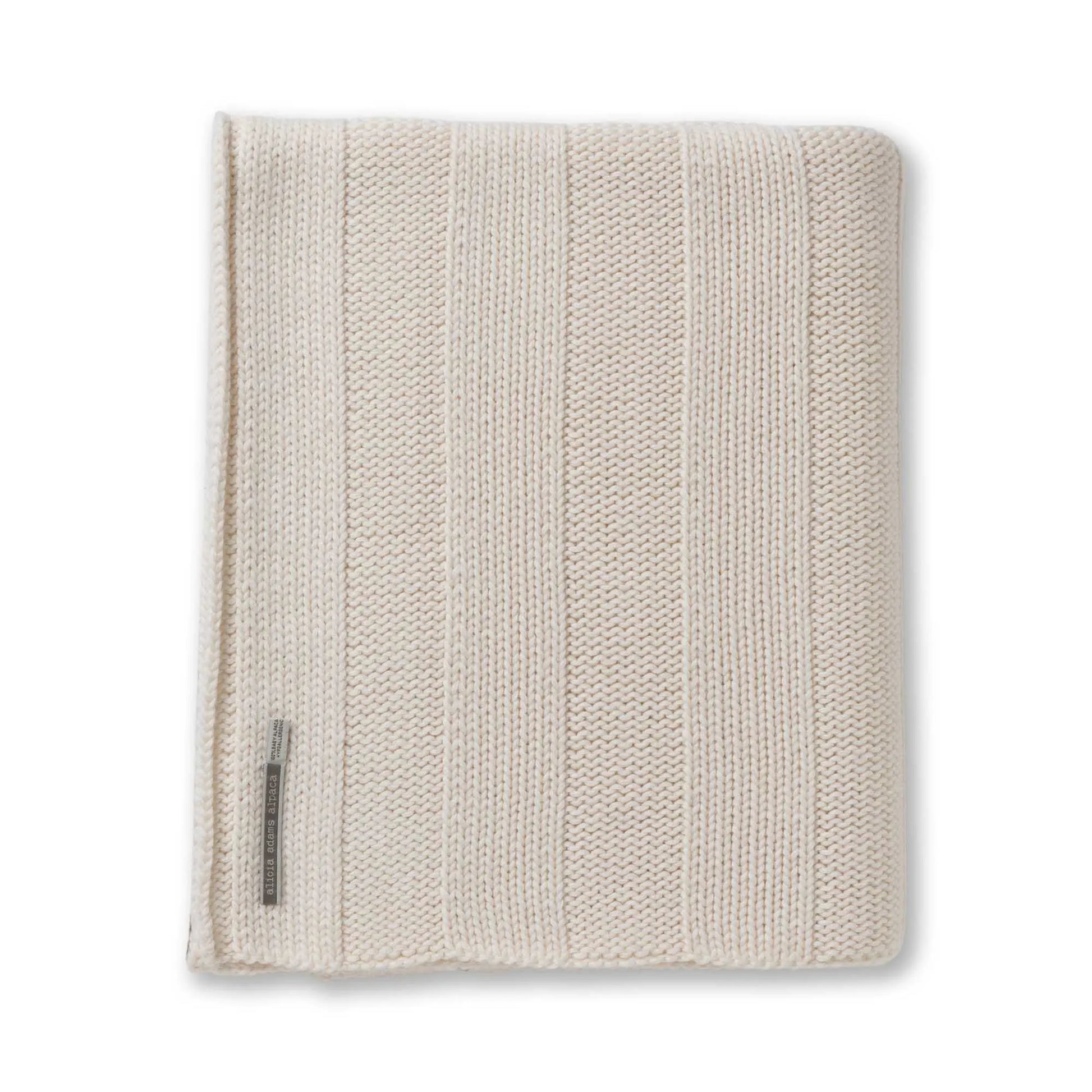 The Garmercy Throw by Alicia Adams Alpaca is a neatly folded, beige and cream striped baby alpaca blanket with a fabric label—luxurious home decor perfect for elevating any space.