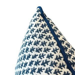 Close-up of the Burma White Indigo Outdoor Pillow by Associated Design, showcasing a blue leaf-like pattern and piped edge on a white background, crafted from premium materials against a plain backdrop.